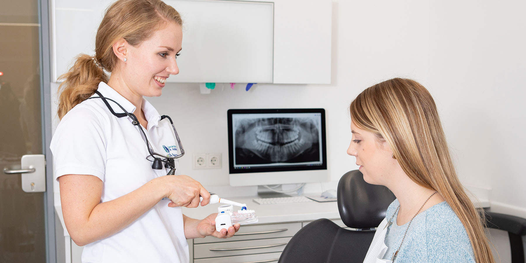 Zahnärztin erklärt Patientin Zahnreinigung mit einem Modell in der Zahnarztpraxis Dr. Frodl