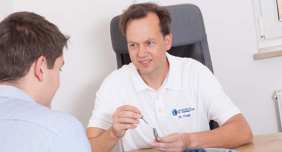 Zahnarzt Frodl aus Landau erklärt einem Patienten ein Implantat