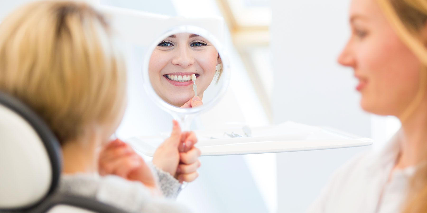 Patientin lächelt im Spiegel in der Zahnarztpraxis Dr. Frodl